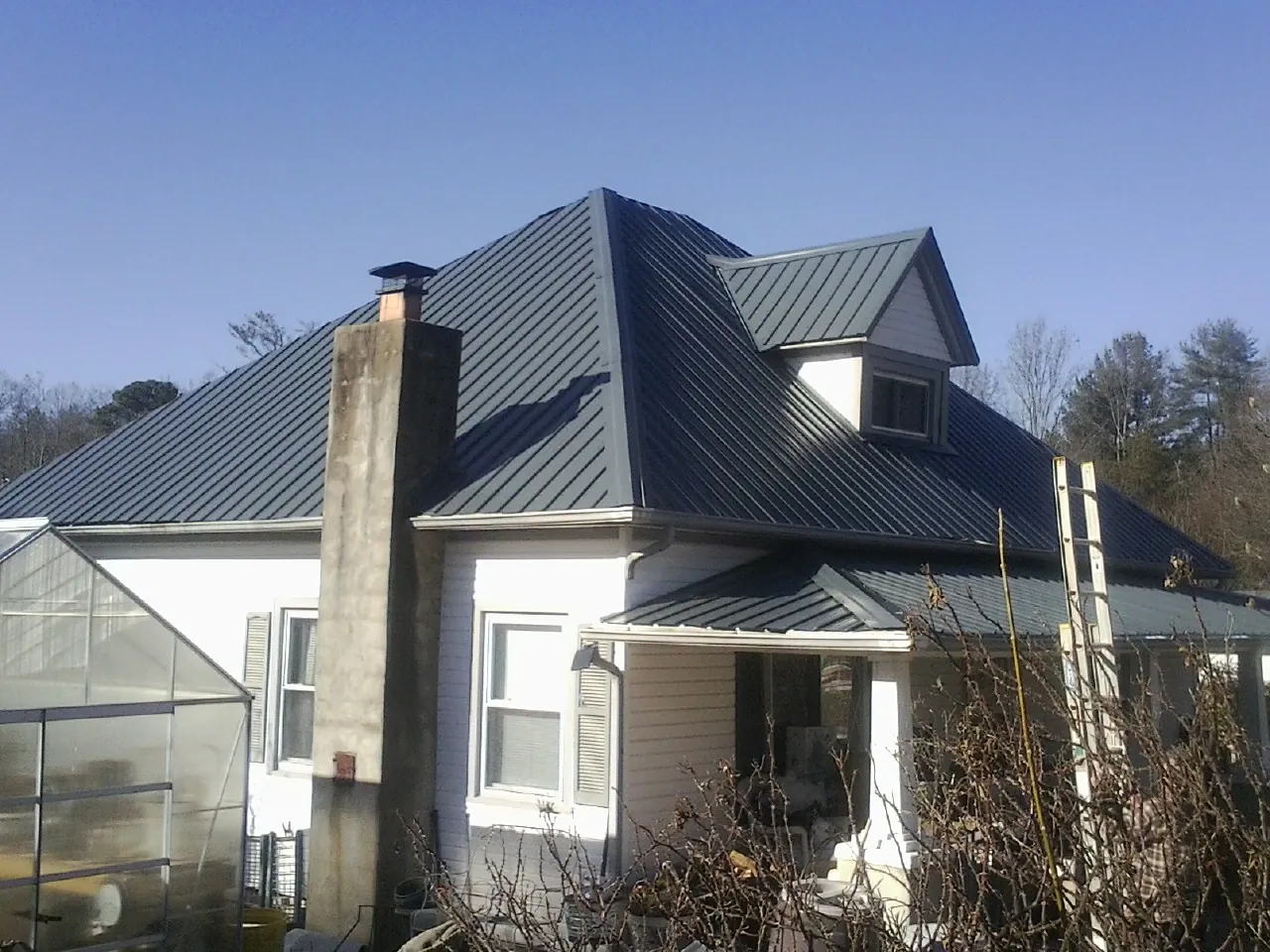 Dark blue standing seam metal roof on a white farmhouse with dormer — Slate & Tile Roof Repair by Roofing Brothers in Laurel Hill