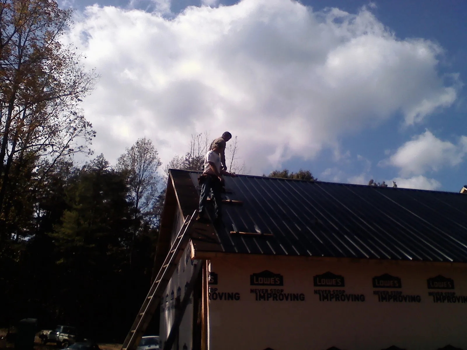 Roofer fastening dark metal panels high against a cloudy sky, from a Roof Inspection job in Laurel Hill